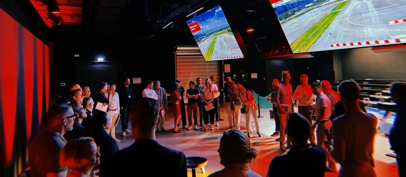 Gruppe von Führungskräften im abgedunkelten Studio, darüber zwei große Leinwände mit der Frage „Where do we grow from here?" über einer Luftaufnahme der Teststrecke