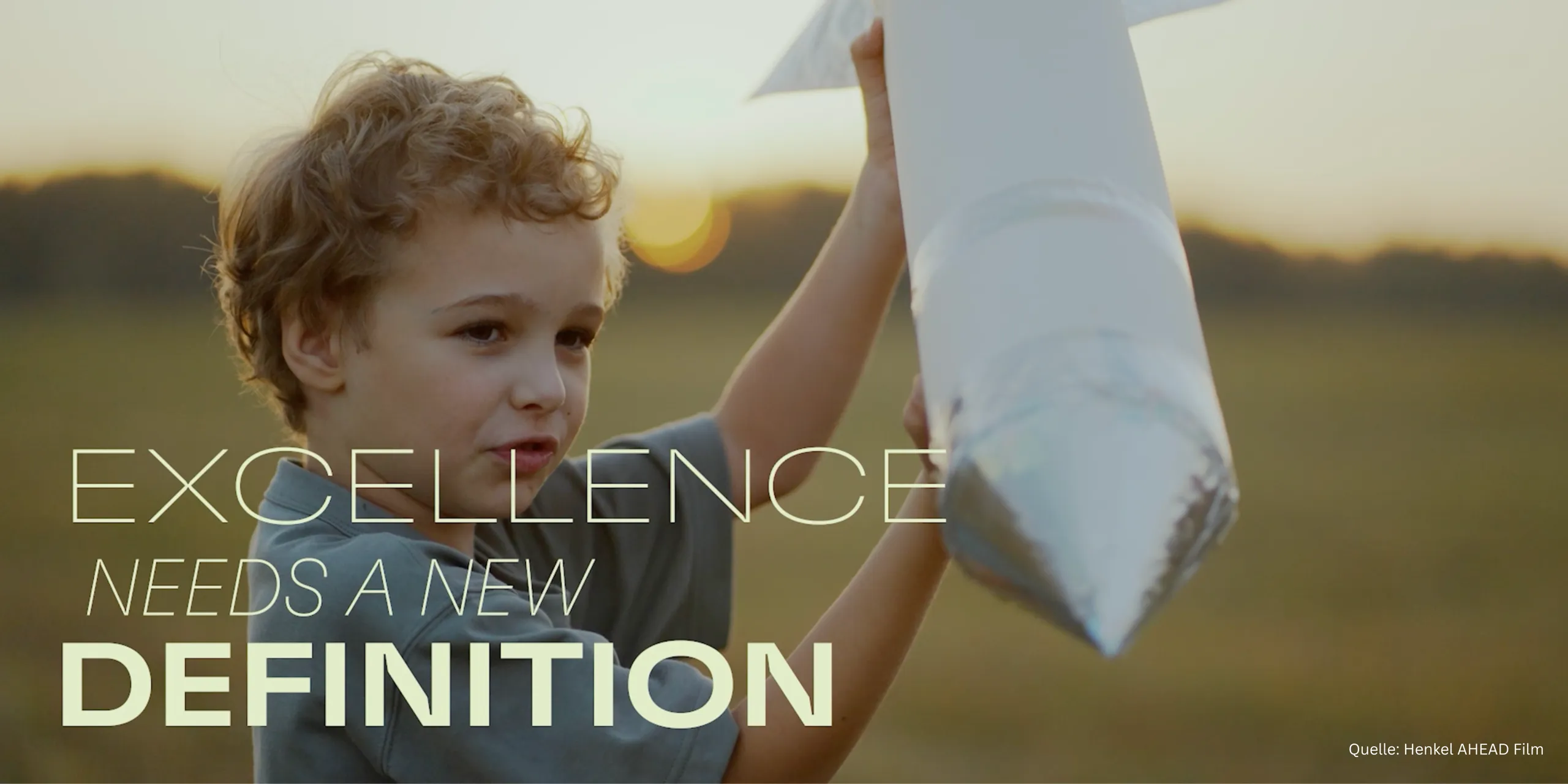 Filmstill aus dem Henkel-AHEAD-Film: ein Junge hält im Abendlicht eine selbstgebaute Papprakete hoch, dazu die Zeile „Excellence needs a new definition“