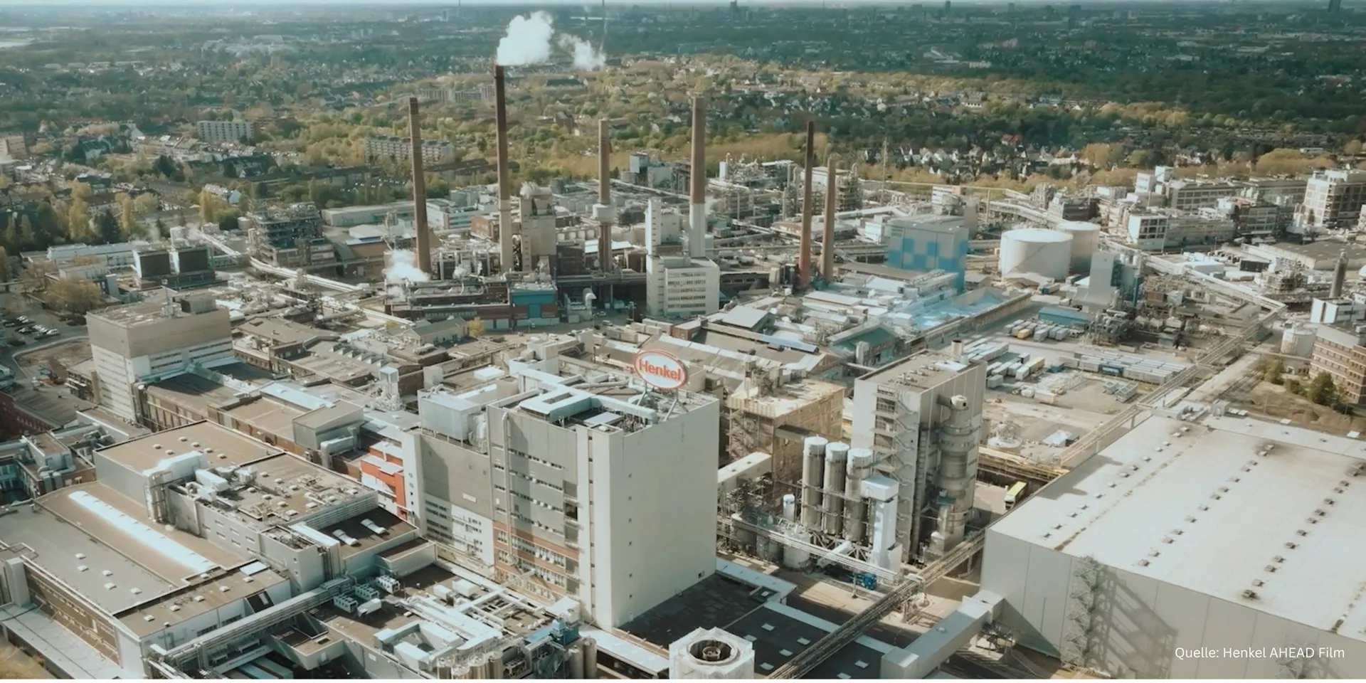 Luftaufnahme des Henkel-Werksgeländes in Düsseldorf mit Schornsteinen und dem roten Henkel-Logo auf einem Hochhaus