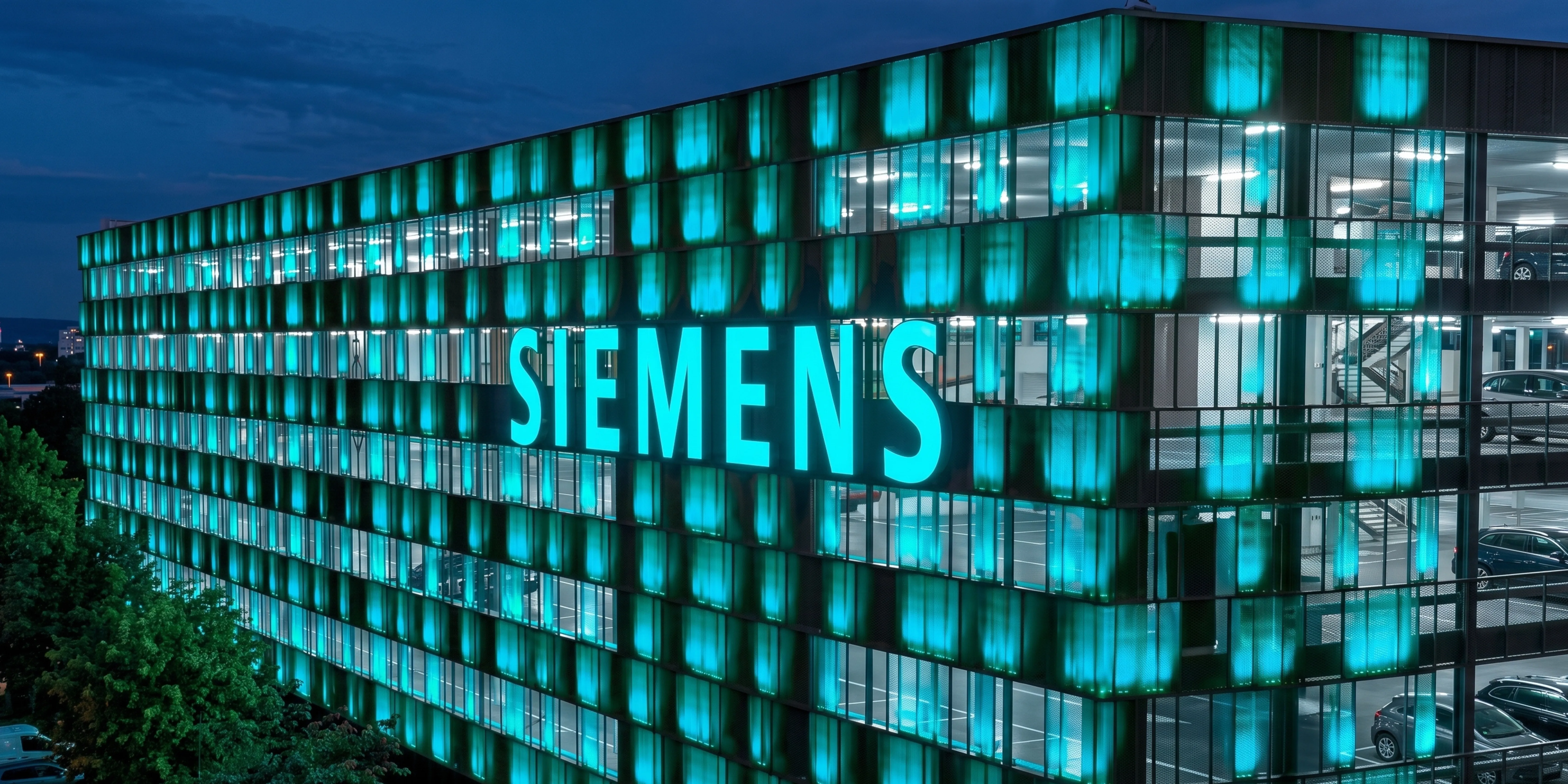 Siemens-Firmengebäude bei Nacht mit beleuchteter Glasfassade und großem SIEMENS-Schriftzug